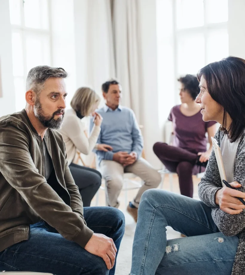 senior-counselor-with-clipboard-talking-to-a-man-during-group-therapy-